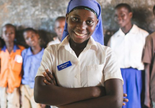 A Ugandan student smiling with her arms crossed looking straight into the camera